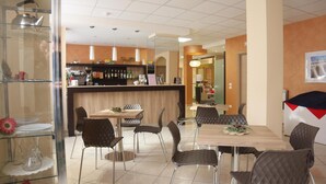 A modern dining area with a bar, wooden tables, and cushioned chairs. - Pensione Piemonte (Loreto)