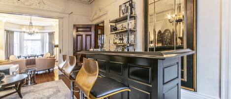 A bar area with high stools, a mirrored wall, and a bookshelf with various items.