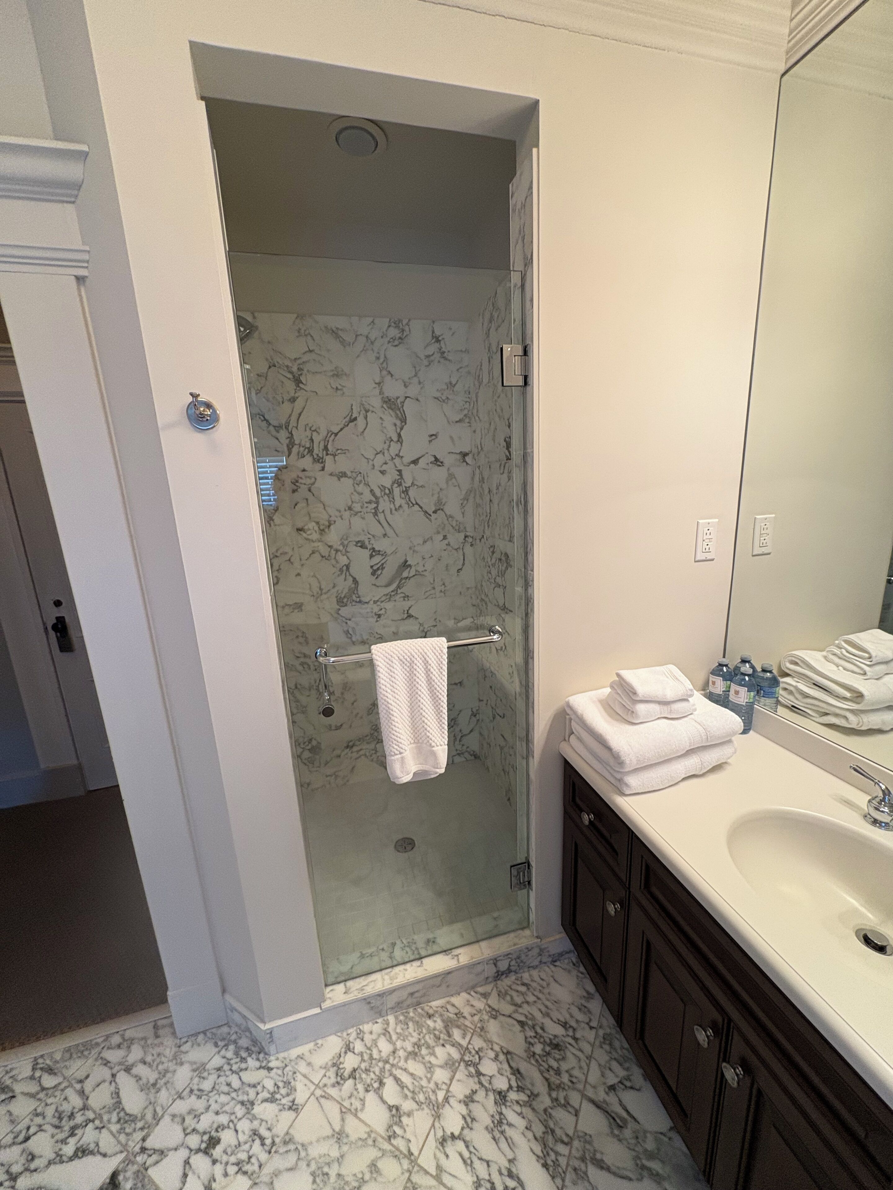 Een badkamer met een glazen douchecabine, een wit wastafelmeubel en een vloer van marmer.