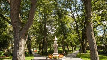 Un sendero bordeado de árboles con un monumento central, rodeado de césped y árboles bien cuidados.