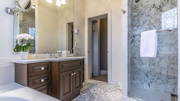 A bathroom with a marble shower, a double sink vanity, and a large mirror.