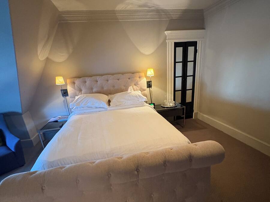 Una cama bien tendida en una habitación de hotel con un ventanal grande, una mesita de noche y una lámpara.