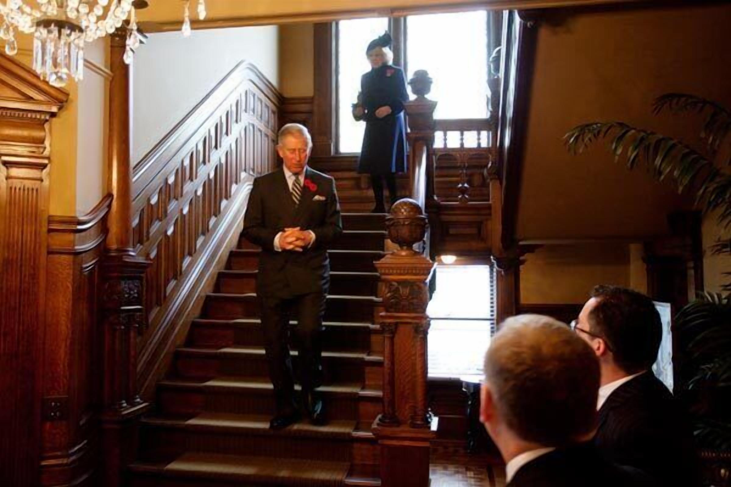 A grand staircase with ornate woodwork and a chandelier, leading to an upper floor.
