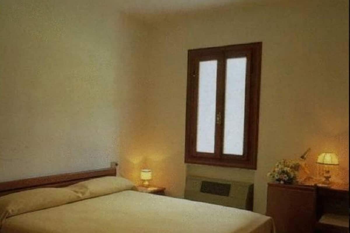 A simple, clean bedroom with a single bed, a nightstand, a desk, and a window.