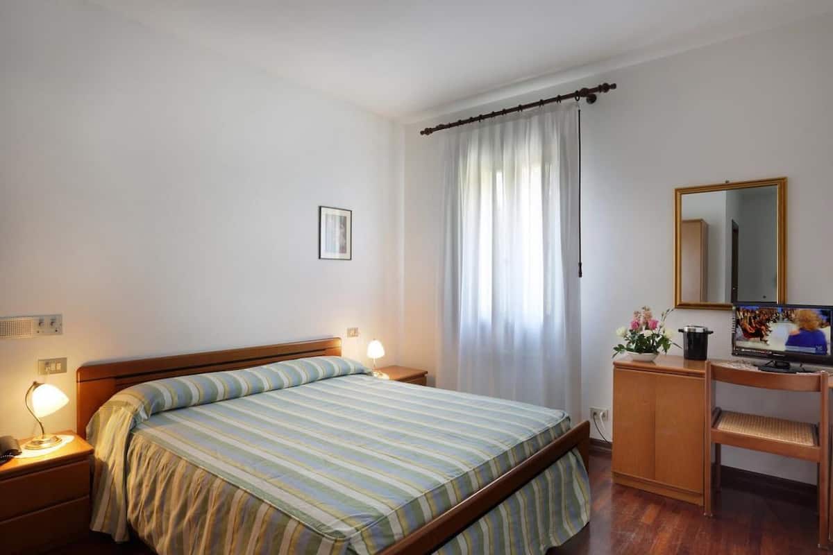 A bedroom with a bed, bedside lamps, a dresser, a mirror, and a television.