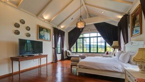 Un dormitorio amplio con una cama grande, un televisor sobre una mesa de madera y vistas al exterior a través de ventanas grandes.