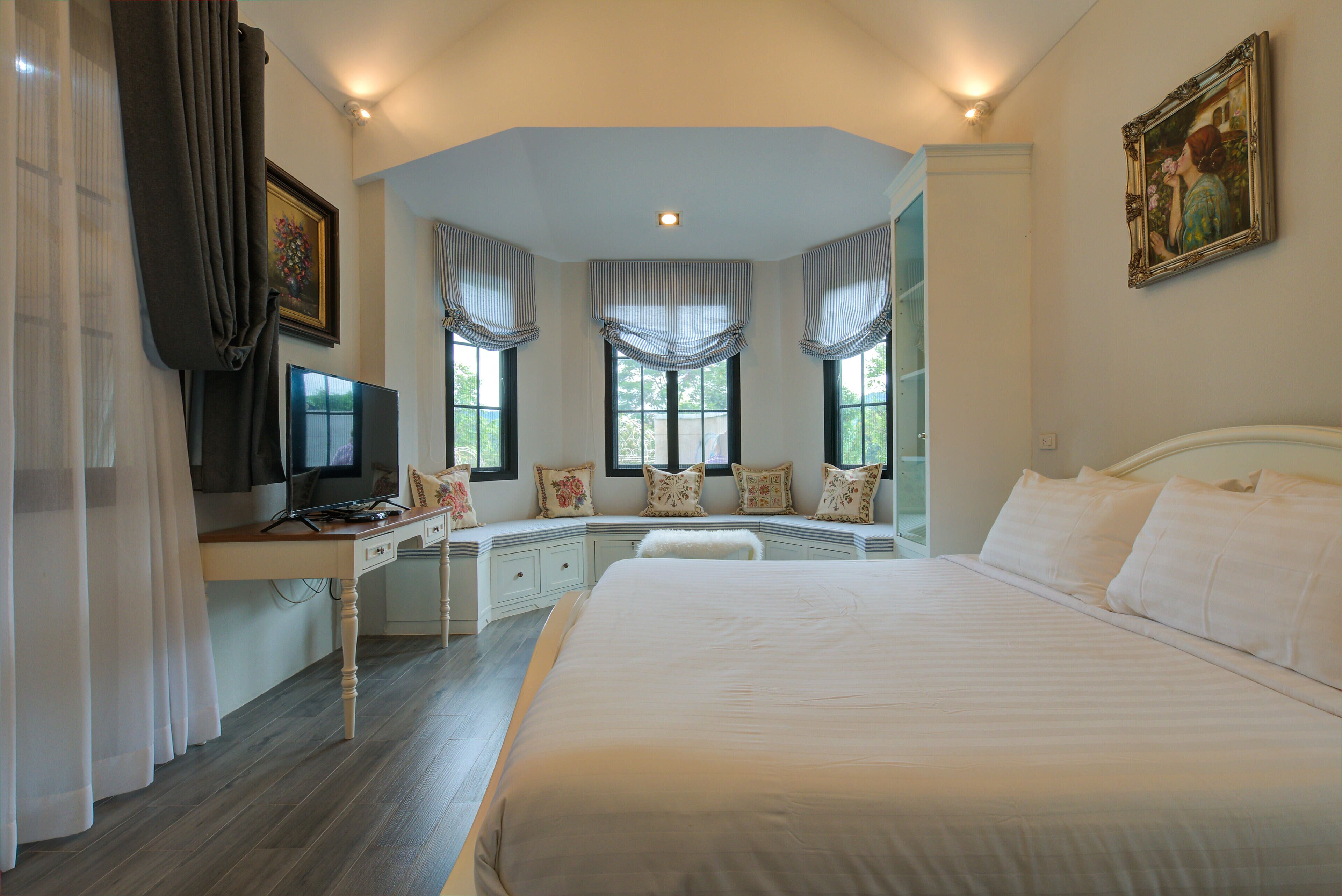 A bedroom with a large bed, a desk with a computer, and a window seat with curtains.