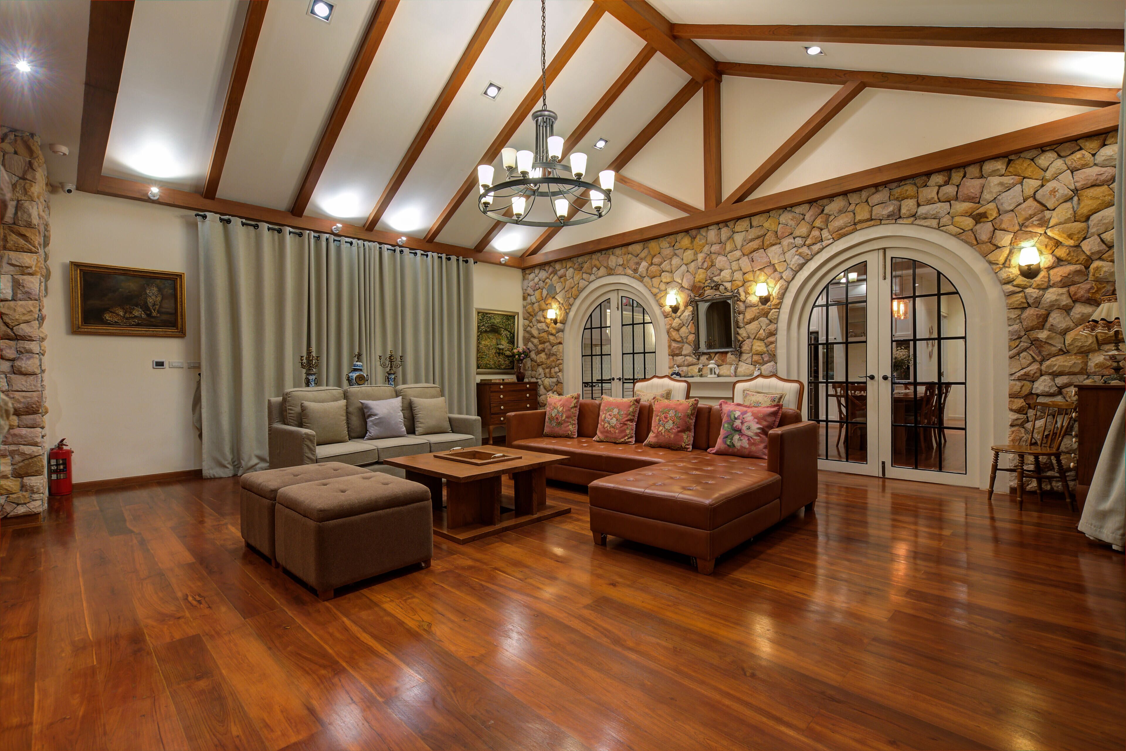 A spacious living room with wooden floors, a stone accent wall, and a large chandelier.