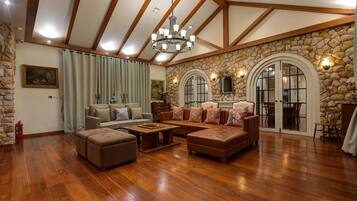 A spacious living room with wooden floors, a stone accent wall, and a large chandelier.