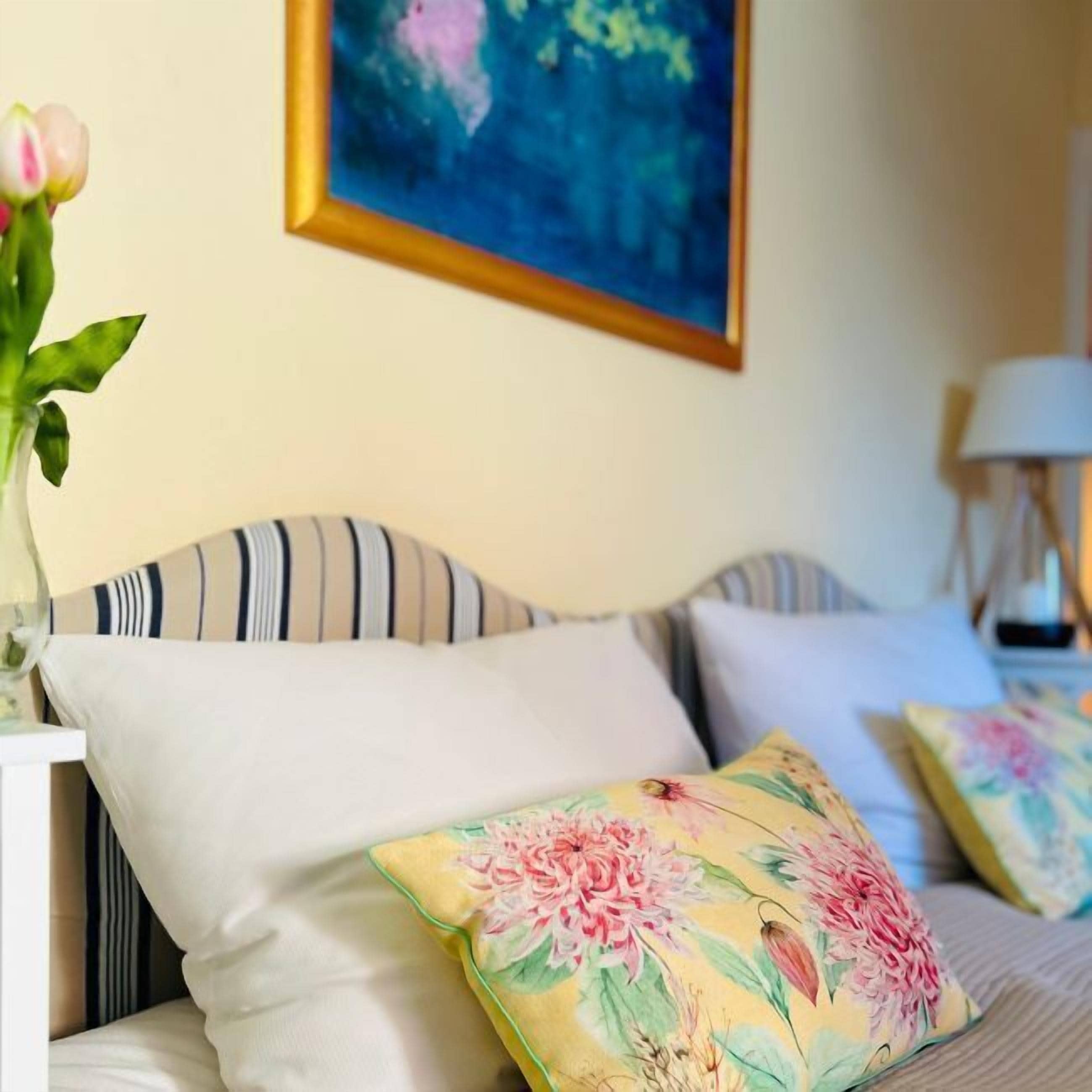 Ein Schlafzimmer mit gestreifter Bettwäsche, einem blumigen Kopfkissen und einem Gemälde an der Wand.