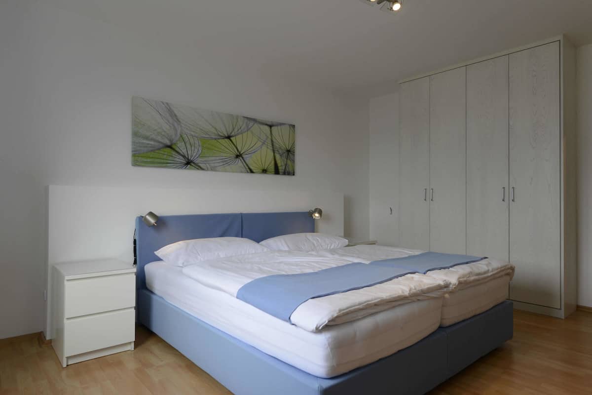 A bedroom with a bed, a nightstand, a wardrobe, and a wall art piece.