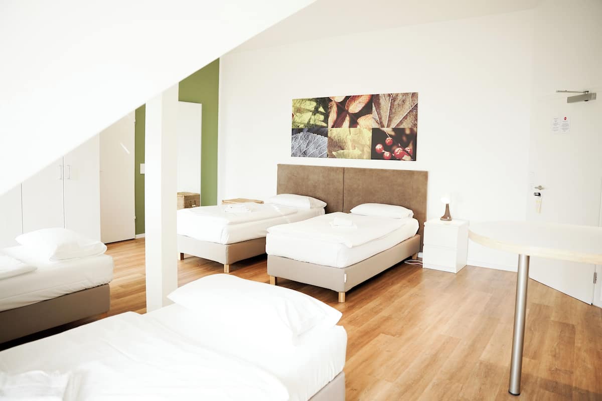 A modern bedroom with two beds, a wooden floor, a painting on the wall, and a small bedside table.