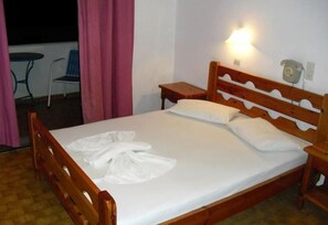 A single bed with wooden headboard and footboard, a bedside table, a lamp, and a telephone on the wall. - Aratos Hotel (Paros)