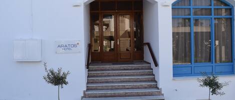 A hotel entrance with a wooden door, a staircase, and two potted plants.