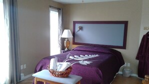 Une chambre d’hôtel avec un grand lit, une table de chevet avec un panier, une lampe et une grande fenêtre avec des rideaux.