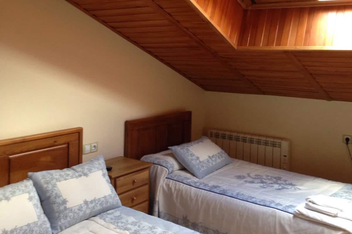 Une chambre avec deux lits, un plafond en bois et une lucarne.