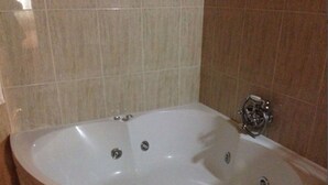 Een groot, ovaal bad met een chromen kraan en meerdere afvoerputjes.