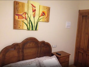 A bedroom with a wooden bed, a nightstand, and a wall-mounted painting of flowers. - Hostal Tribal (Puebla de Sanabria)