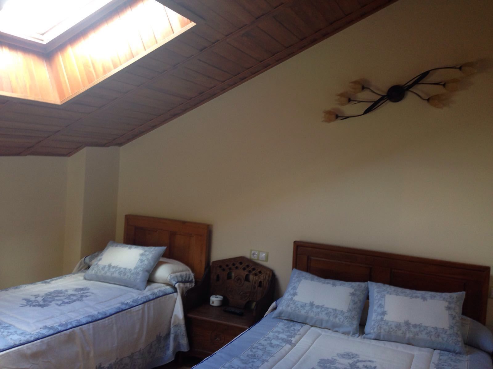 A bedroom with two beds, a skylight, a wooden ceiling, and a wall-mounted light fixture.