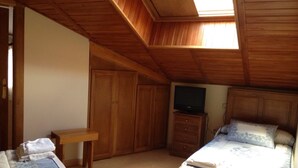 Een slaapkamer met een schuine plafond, een houten garderobe, een televisie op een houten standaard, een bed met een bloemenprint sprei en een bankje met handdoeken.