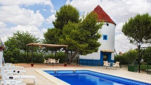 Un espace piscine avec des chaises longues, un coin salon abrité et un bâtiment doté d’un toit rouge.