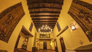 Un vaste hall d’entrée avec un plafond en bois, des peintures murales décoratives et un lustre.