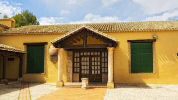 A building with a tiled roof, a central entrance with a wooden door, and green shutters on the windows.