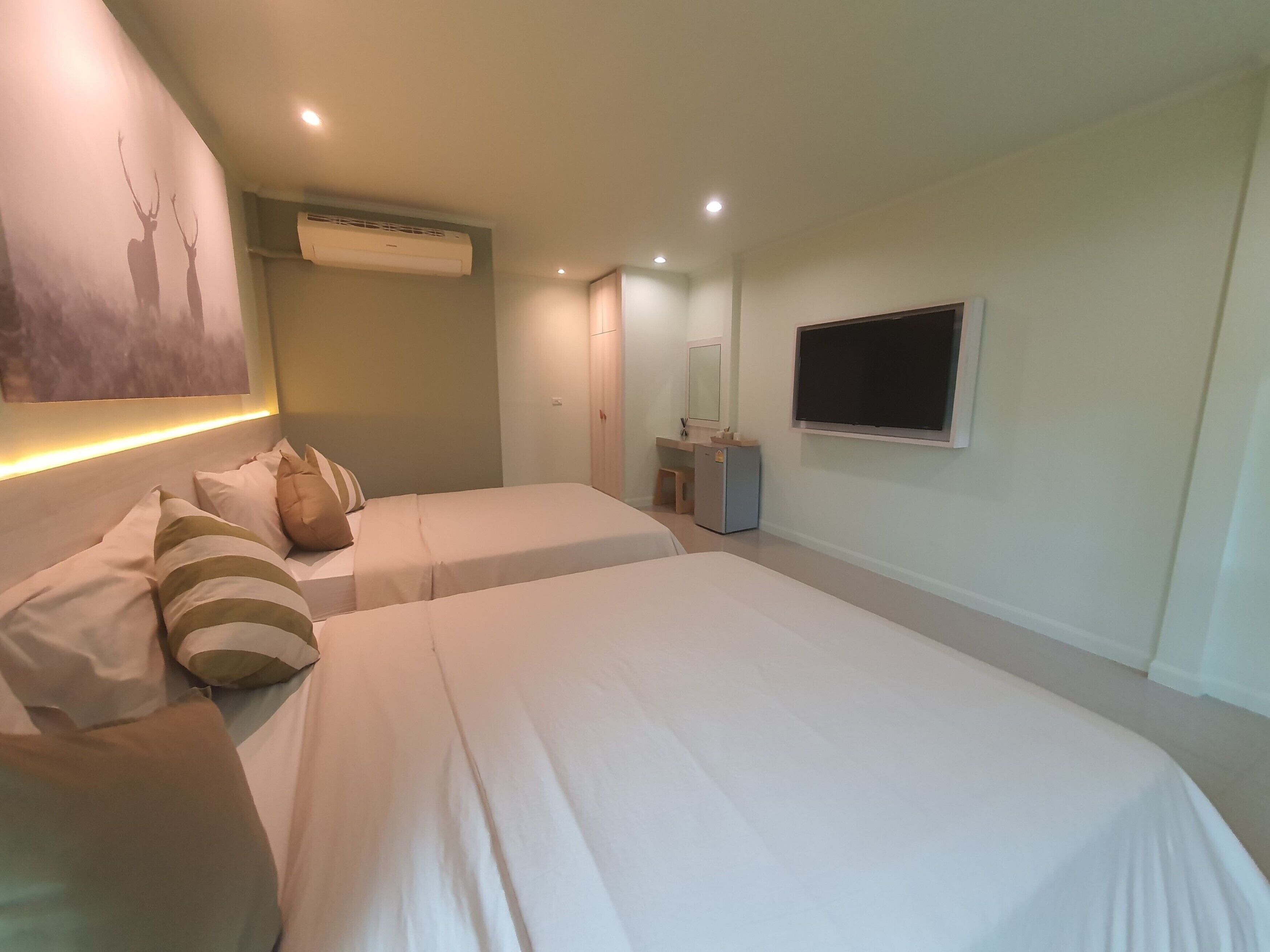 A hotel room with two beds, a desk, a mirror, an air conditioner, and a TV.