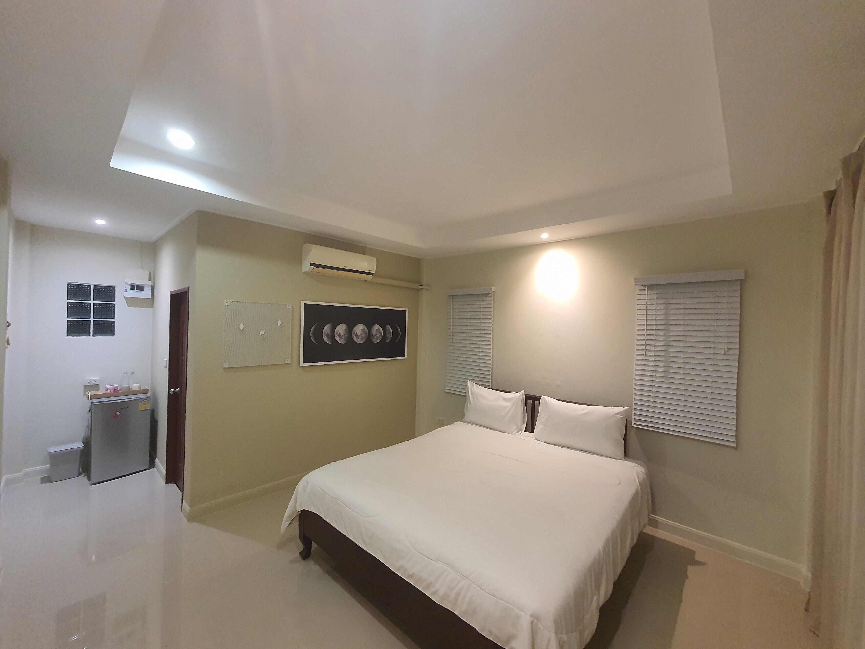 A bedroom with a bed, a wall-mounted air conditioner, a window with blinds, and a small cabinet with toiletries.