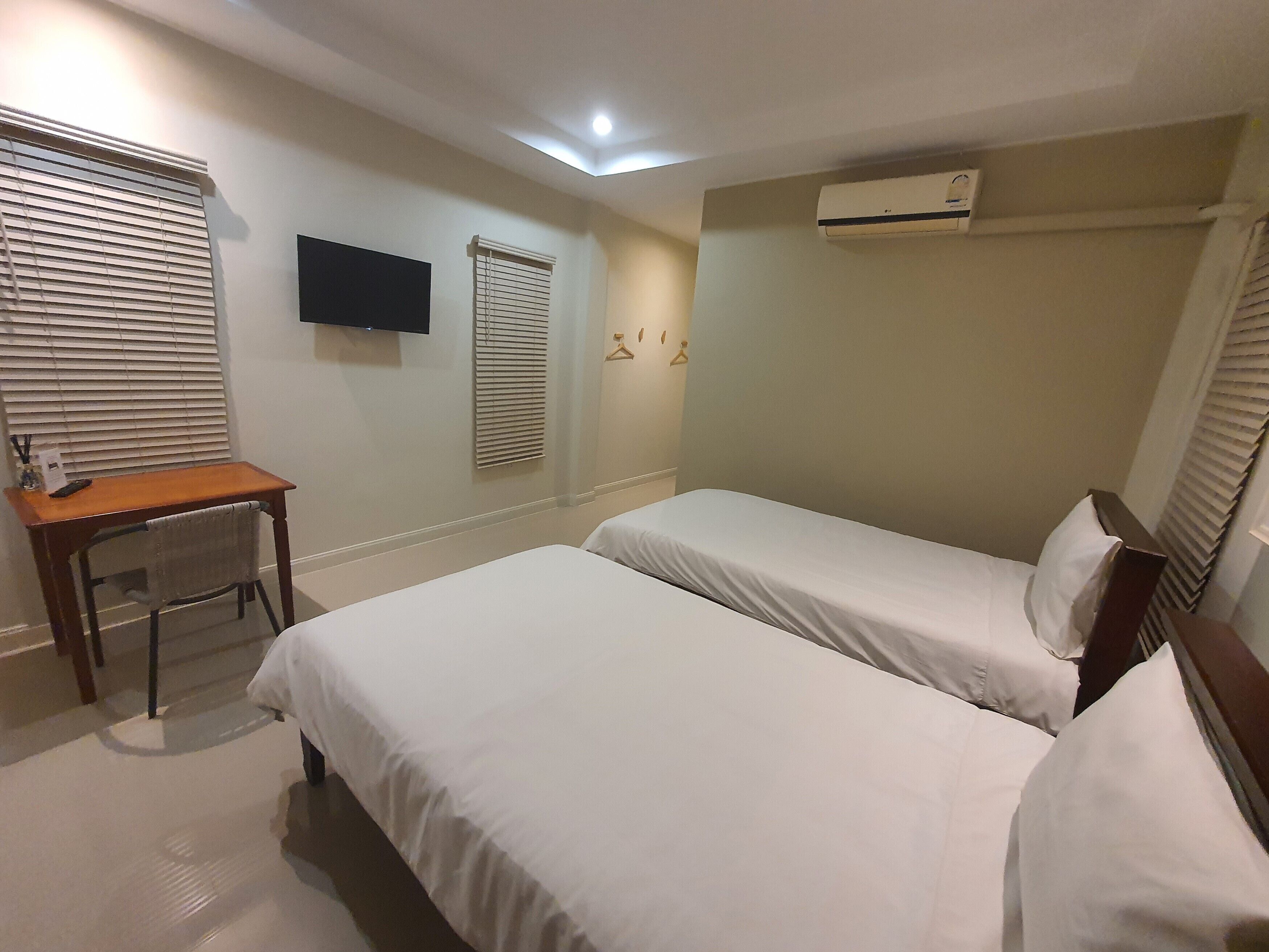A hotel room with two single beds, a desk with a chair, a flat-screen TV mounted on the wall, and an air conditioning unit.