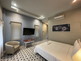 Habitación de hotel con cama, televisión, una silla y un cuadro en la pared.