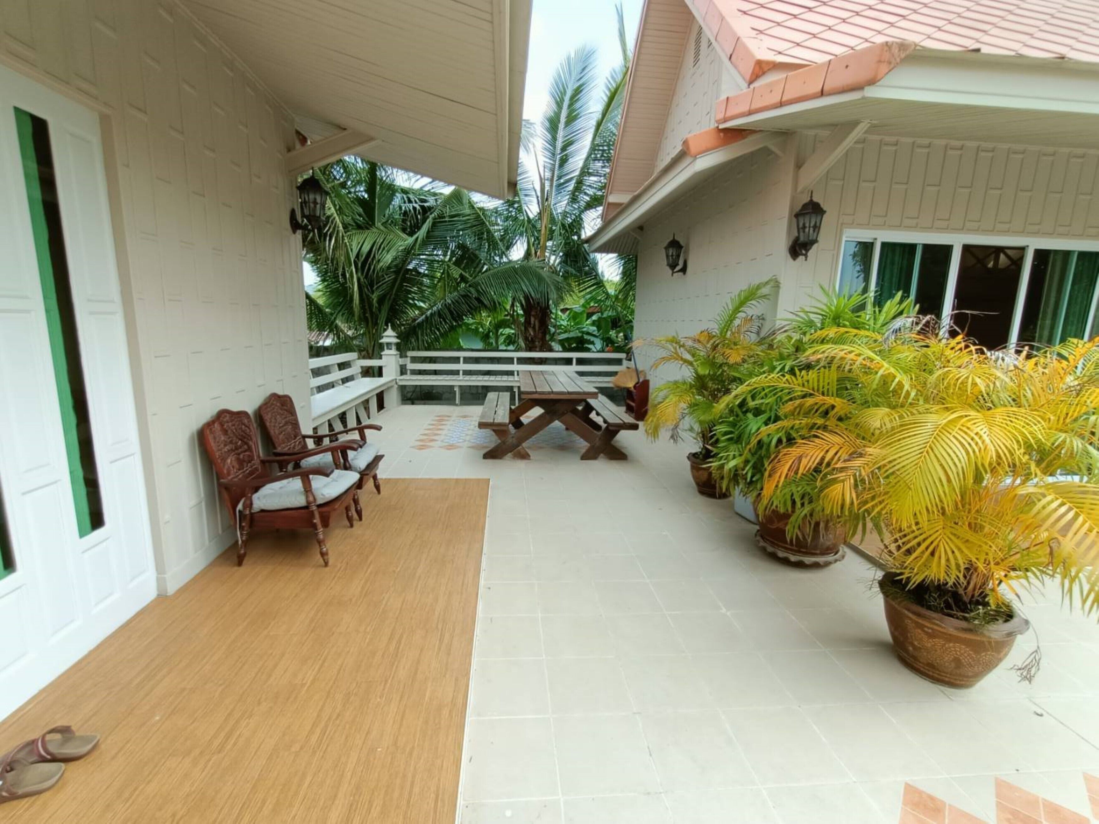 A covered patio area with wooden furniture, potted plants, and a view of the surrounding greenery.