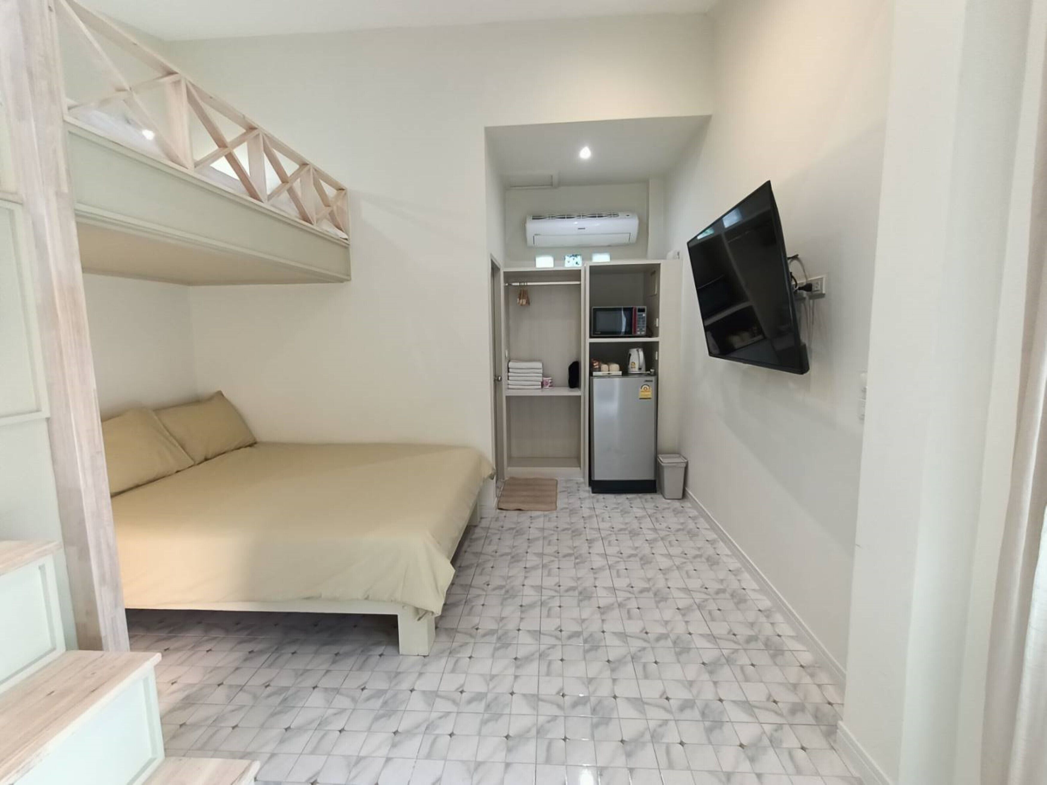 A compact bedroom with a bunk bed, a built-in wardrobe, a small kitchenette, and a TV mounted on the wall.