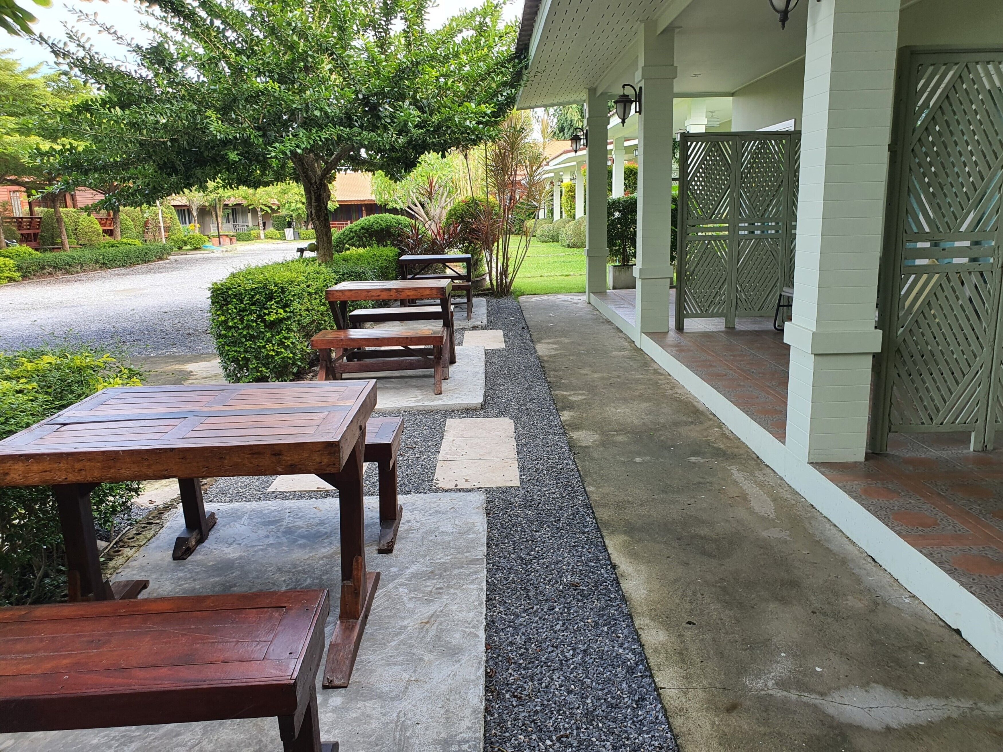 An outdoor seating area with wooden tables and benches, a gravel path, and a green fence.