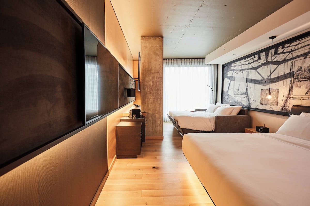 A modern hotel room with a large bed, a smaller bed, a desk, and a large mirror.