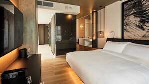 Un moderno cuarto de hotel con una cama grande, un televisor de pantalla plana, una cafetera y un cuadro de gran tamaño en la pared.