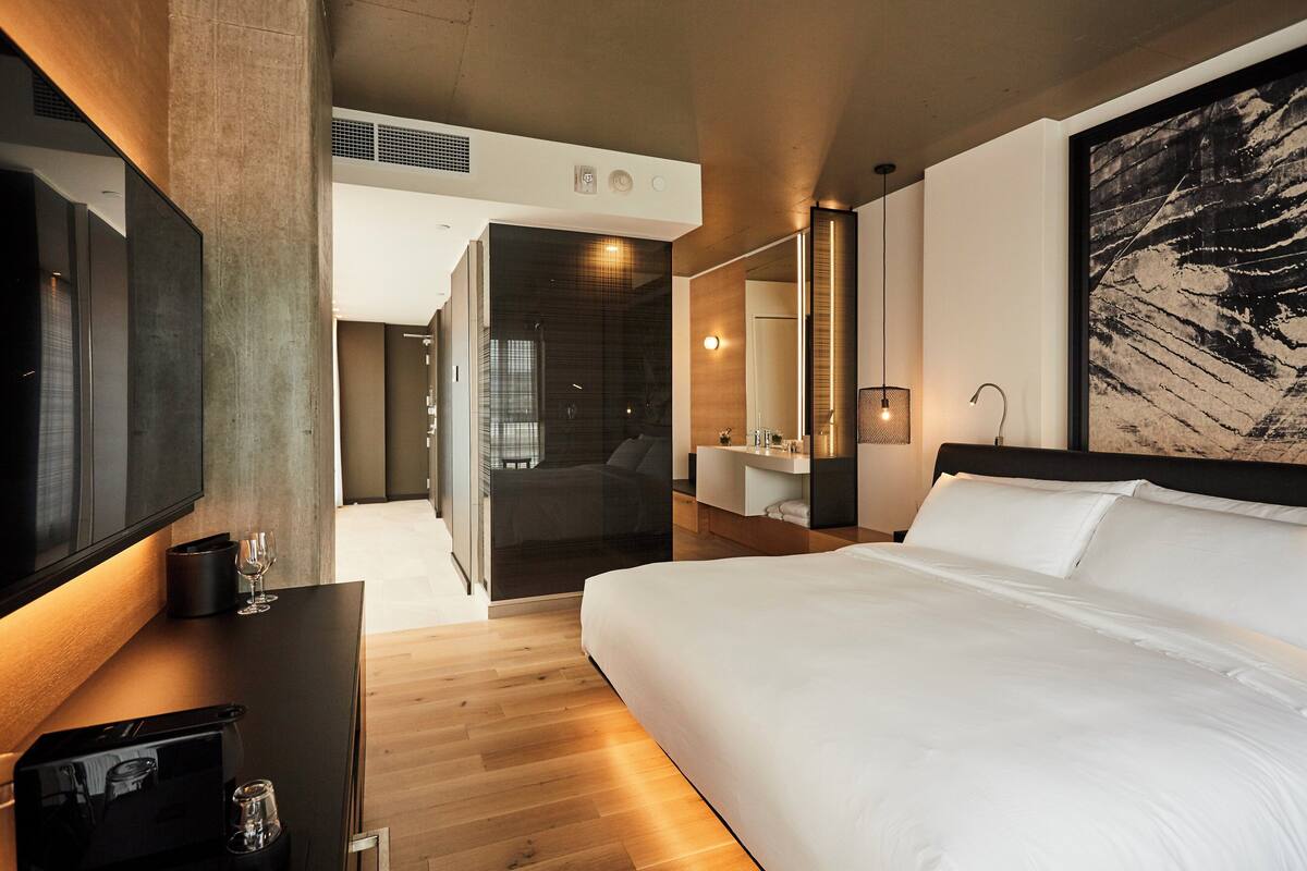 A modern hotel room with a large bed, a flat-screen TV, a coffee machine, and a large painting on the wall.