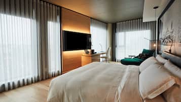 Ett modernt hotellrum med en stor säng, ett skrivbord med en platt-TV och en bekväm sittgrupp med en fåtölj och en soffa.
