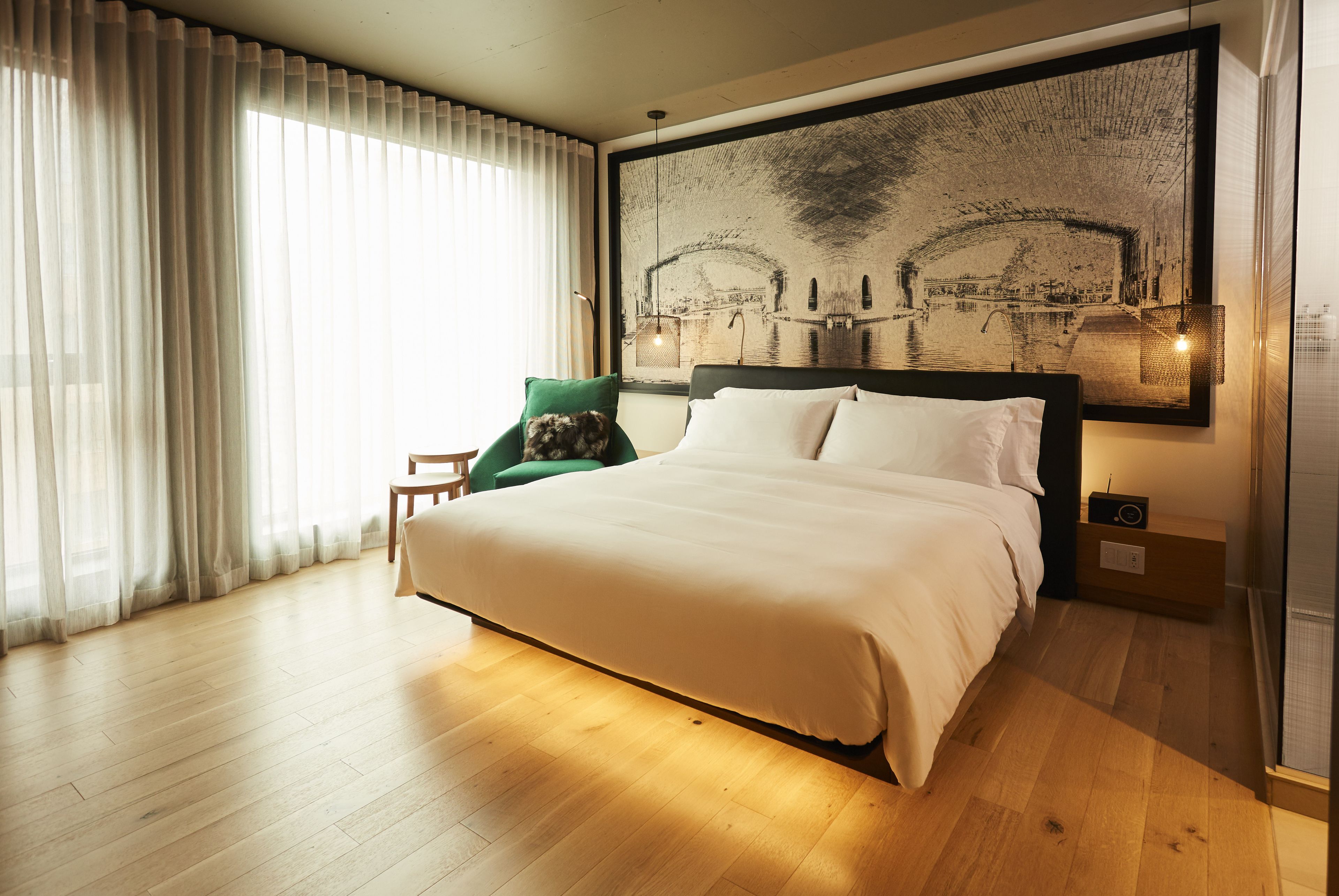 A neatly made bed with white linens, a green chair, and a large framed picture above the bed.