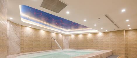 Un espace spa moderne doté d’un jacuzzi, de quelques marches menant au jacuzzi et d’un plafond agrémenté d’un système d’éclairage décoratif.