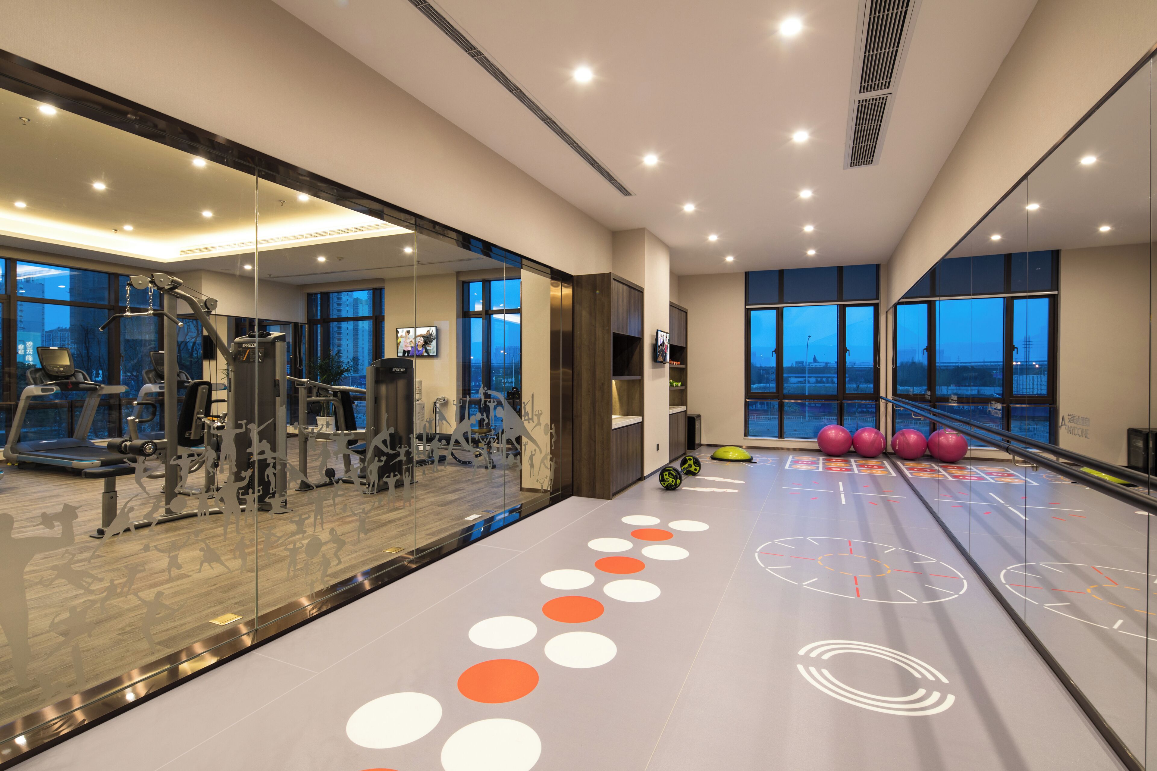 A modern gym with exercise equipment, large windows, and a mirrored wall.