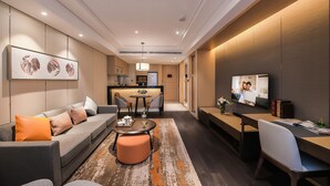 Una habitación de hotel moderna con sofá, reposapiés, mesa de comedor y televisor.