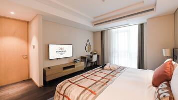 A hotel room with a bed, a TV, a desk, and a window with curtains.