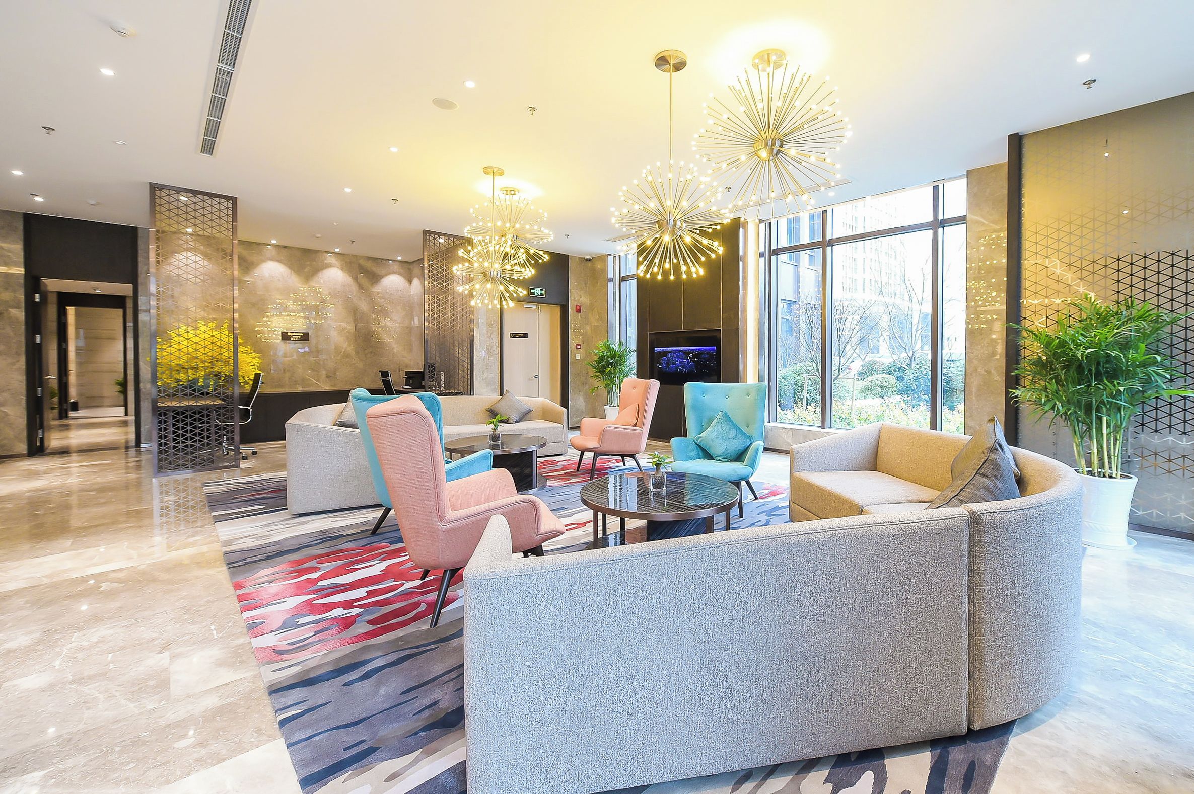 Een moderne lobby met een zithoek, grote ramen en decoratieve verlichting.