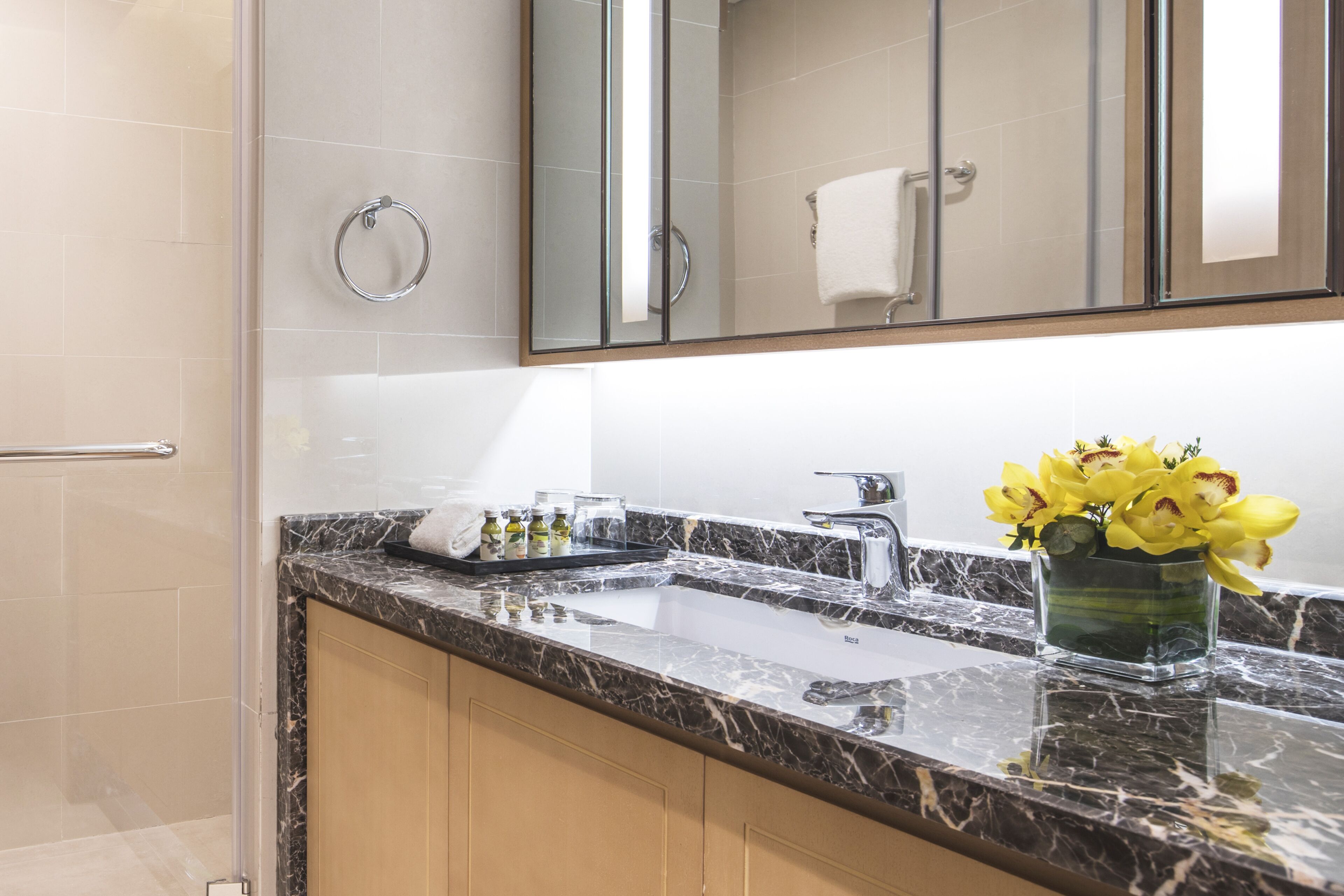 Un baño moderno con lavamanos de mármol, cabina de ducha de vidrio y un espejo grande.