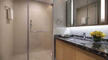 Un baño moderno con ducha de vidrio, lavamanos de mármol y un espejo sobre el mueble.