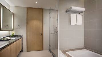 A modern bathroom with a glass-enclosed shower, a wooden door, a marble countertop, and a white bathtub.