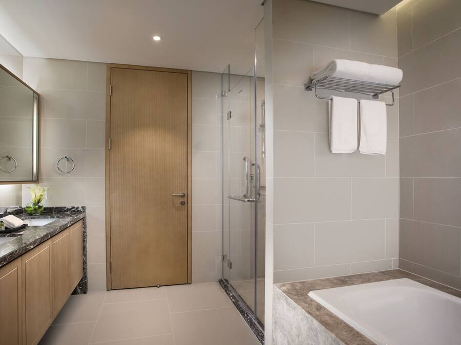A modern bathroom with a glass-enclosed shower, a wooden door, a marble countertop, and a white bathtub.