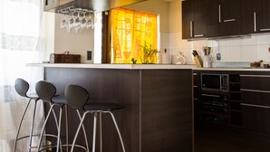 Une cuisine moderne avec des meubles de couleur bois foncé, un îlot central doté de tabourets, un téléviseur à écran plat et une fenêtre avec des rideaux.