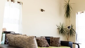 Un salon avec un plafond haut, un canapé orné de coussins à motifs et deux plantes en pot.